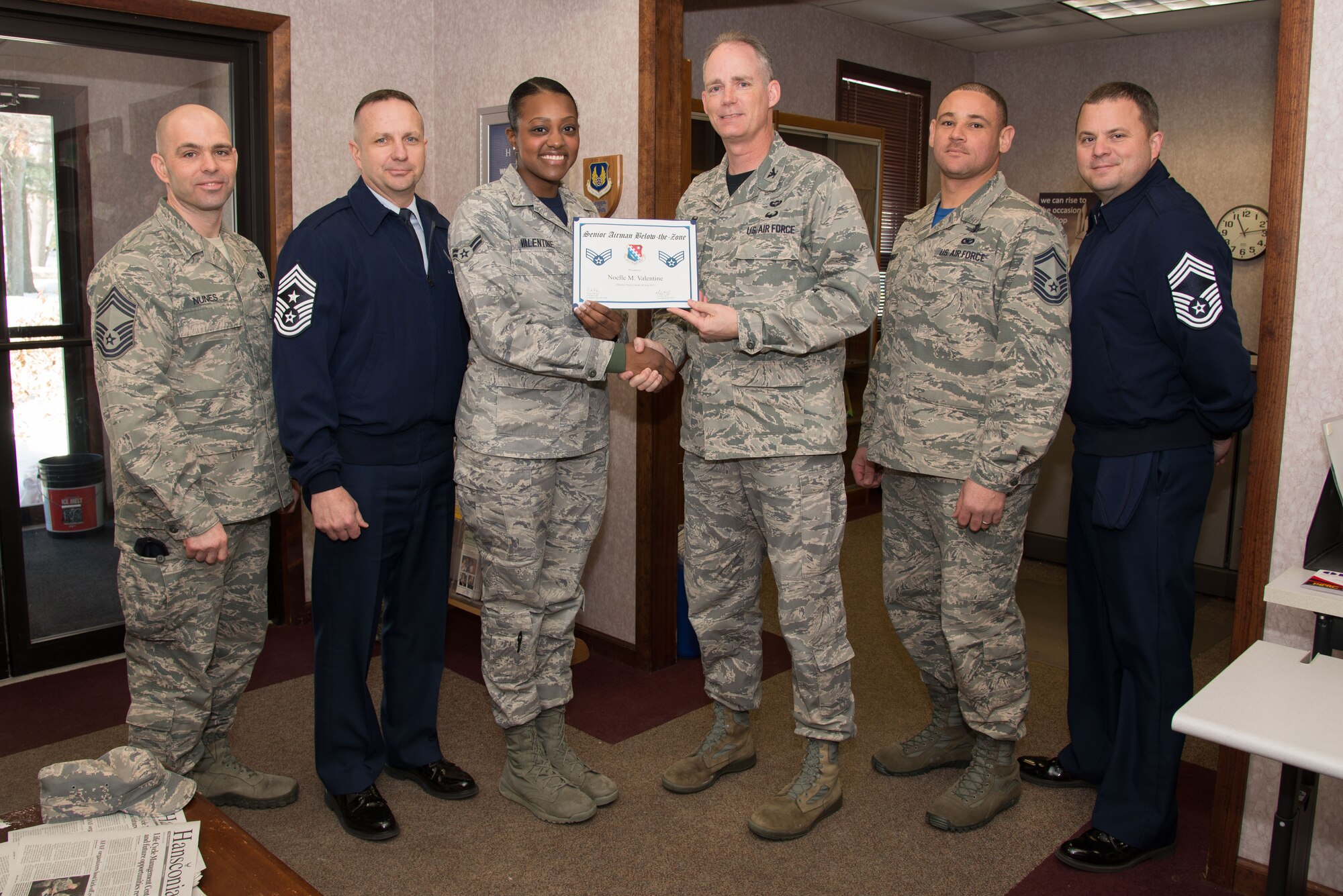 66th Air Base Group Commander Col. Michael A. Vogel and Hanscom Command Chief Master Sgt. Craig A. Poling and other enlisted senior leaders present newly promoted Senior Airman Noelle Valentine, Air Force Life Cycle Management Center Detachment 7, with a certificate for a below-the-zone promotion to senior airman at her office on base March 13. Valentine and five others met a BTZ promotion board earlier in the day for the early promotion. BTZ is a competitive early promotion program offered to those in the rank of airman first class who stand out from their peers. (U.S. Air Force photo by Mark Herlihy)