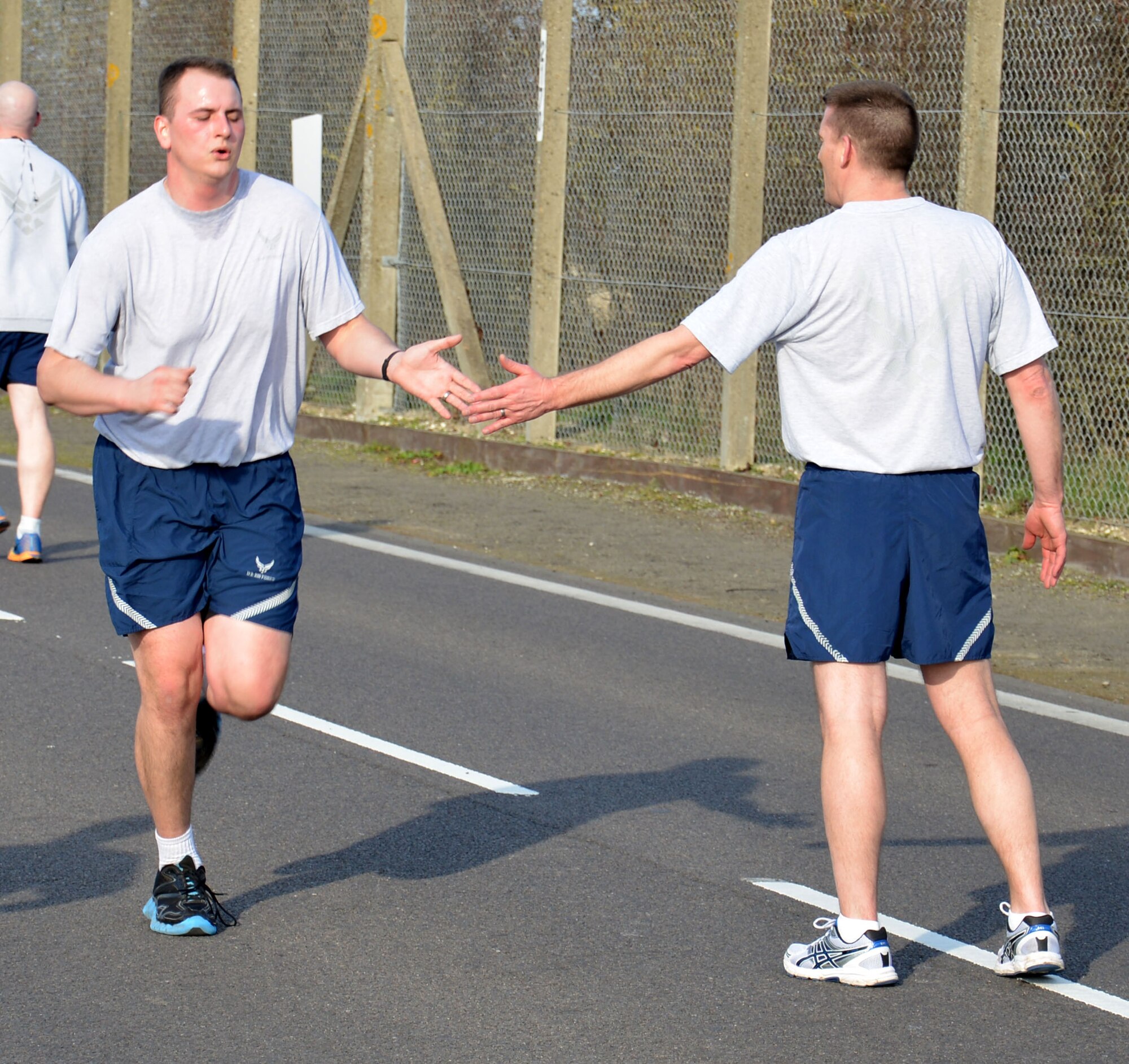U.S. Air Force Chief Master Sgt. Tracy Jones, right, 100th Air Refueling Wing command chief, congratulates Team Mildenhall members as they cross the finish line during a monthly wing run March 13, 2015, near the Hardstand Fitness Center on RAF Mildenhall, England. The monthly 5k run brings together many units on base through exercise and healthy competition. (U.S. Air Force photo by Gina Randall/Released)