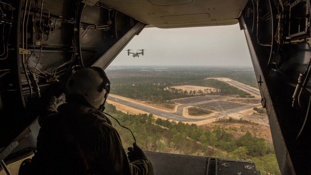 A crew chief with Marine Medium Tiltrotor Squadron 261 monitors another MV-22B Osprey and the ground below during a division flight exercise in the Camp Lejeune vicinity, March 3, 2015. Crew chiefs responsibilities include loading and balancing cargo and making adjustments to electrical systems while in flight. 