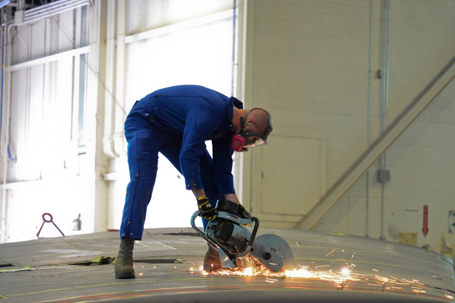 An Airman from the 5th Maintenance Squadron repair and reclamation section uses an electric saw to cut the vertical fin of a B-52H Stratofortress on Minot Air Force Base, N.D., Feb. 25, 2015. The fin is being cut for shipping purposes for thermal and blast testing. Thermal testing will look at the thermal response of coatings and material stack-ups to a pulse similar to a nuclear thermal pulse. Blast testing will be conducted at a future date looking into the structural response to an overpressure shockwave. The results will be used to update the nuclear hardness of the aircraft, which is used in models to produce Escape Distance Required Curves within Technical Order 25s. (U.S. Air Force photo/Senior Airman Brittany Y. Bateman)