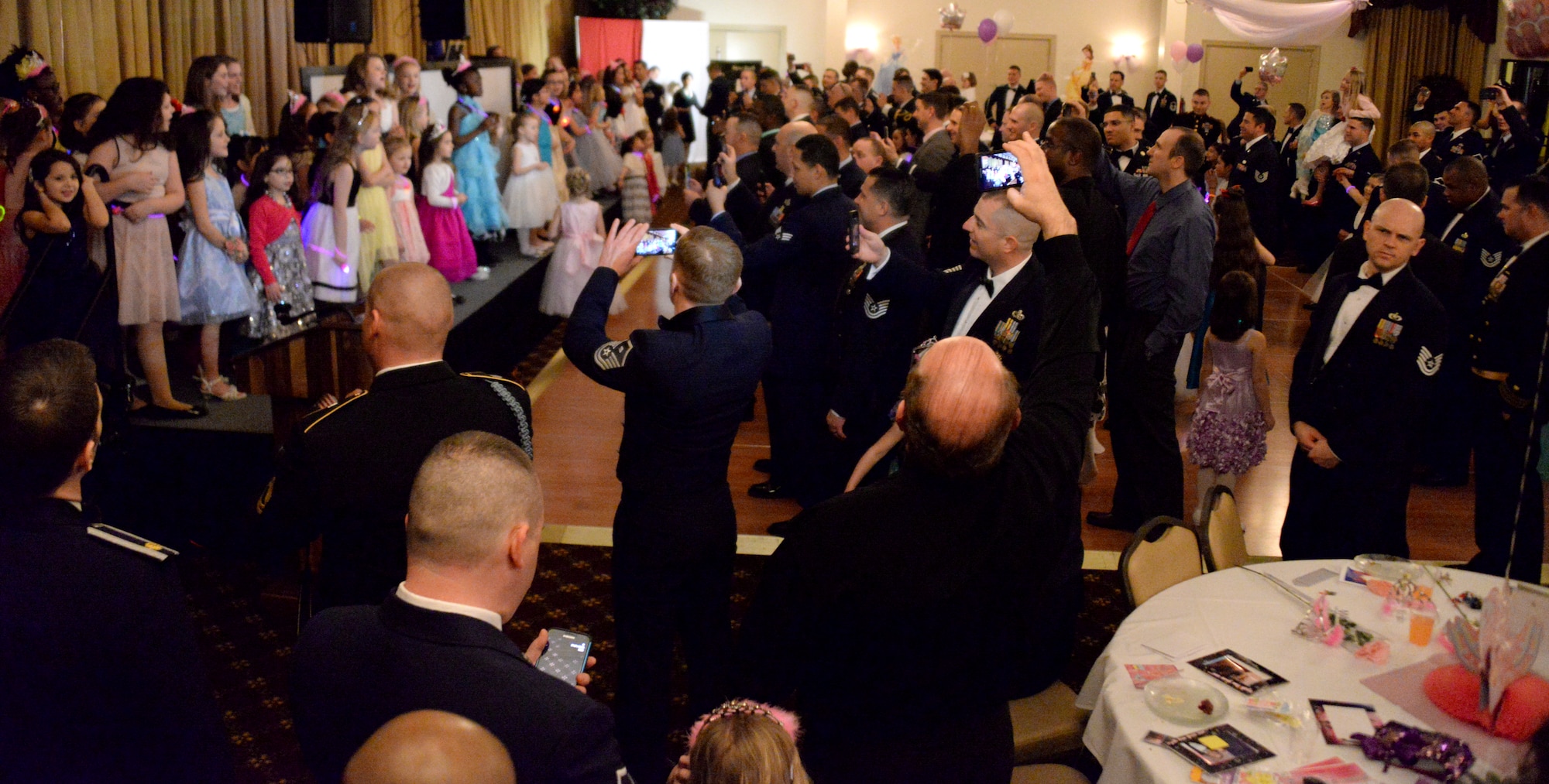 Fathers group together to record their daughters singing the popular Disney song “Let It Go,” during the Annual Princess and Her Hero Dance at Tommy B’s Community Activities Center on Joint Base McGuire-Dix-Lakehurst, N.J., March 13, 2015. The dance is held each year for young girls and their fathers to share a special evening together, while showing young girls a positive male role model. (U.S. Air Force photo by Airman 1st Class Tara A. Williamson/Released)