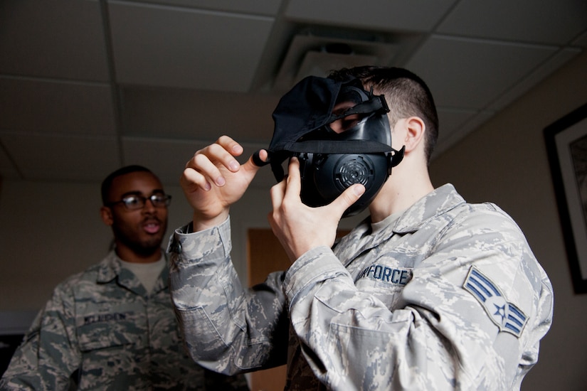 Senior Airman Thomas Hollingsworth, 779th Aerospace Medicine Squadron bioenvironmental technician, demonstrates putting on a gas mask with the help of Airman 1st Class Ashton McLaughlin, 779th AMS bioenvironmental technician, March 16, 2015, on Joint Base Andrews, Md. The flight conducts approximately 1,400 gas mask fit tests and tests more than 140 water samples per year.  (U.S. Air Force photo/Senior Airman Mariah Haddenham)