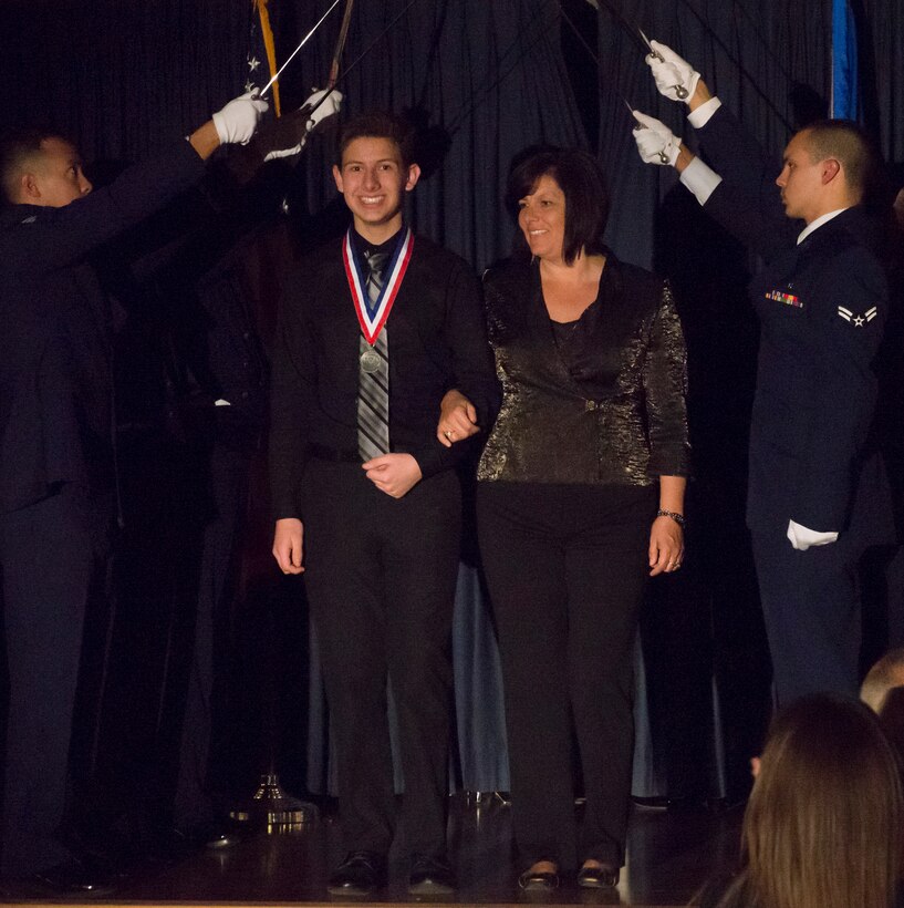 Nicholas Parkinson takes the stage with his mother Leila Parkinson during the Annual Awards ceremony at Mountain Home Air Force Base, Idaho, Feb. 18, 2015. Nicholas was recognized as the youth volunteer for the wing during the first and fourth quarter. (U.S. Air Force photo by Airman 1st Class Jessica H. Smith/RELEASED)