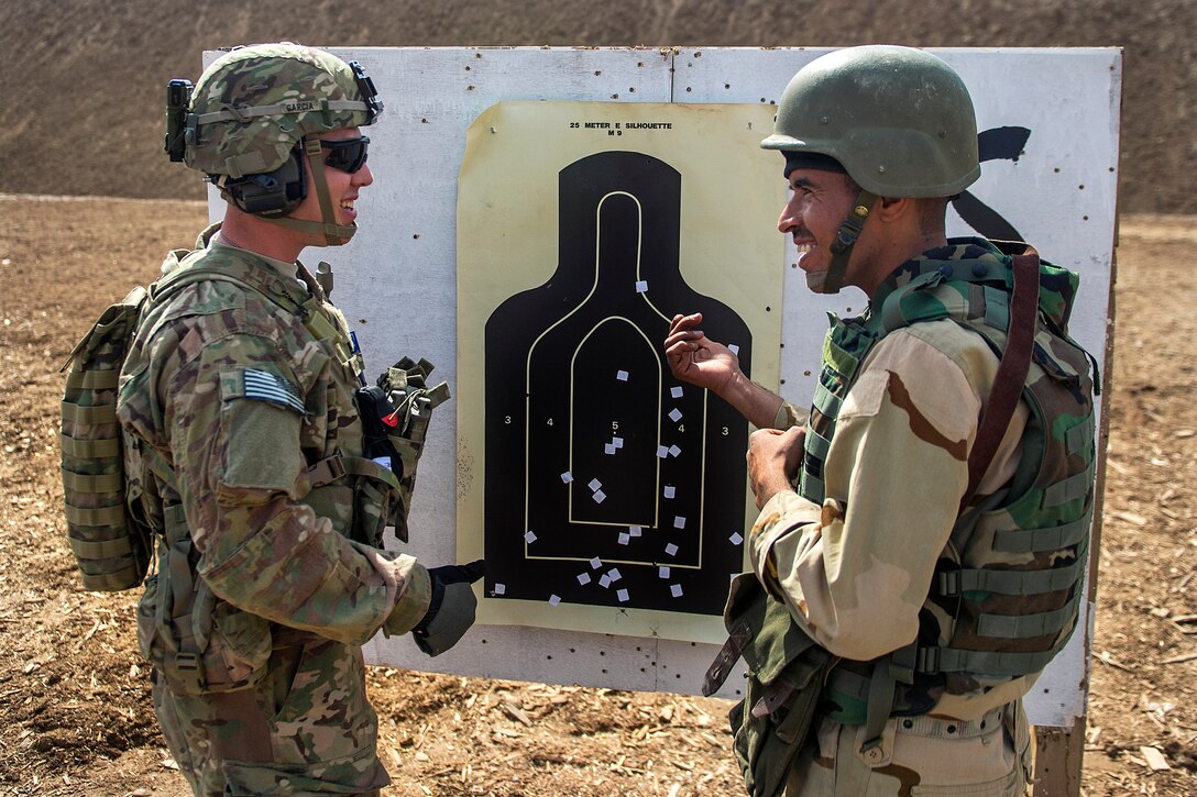 U.S. Army Spc. Tony Garcia, left, talks to an Iraqi soldier about his shot groupings during a weapons qualification on Camp Taji, Iraq, March 8, 2015.
