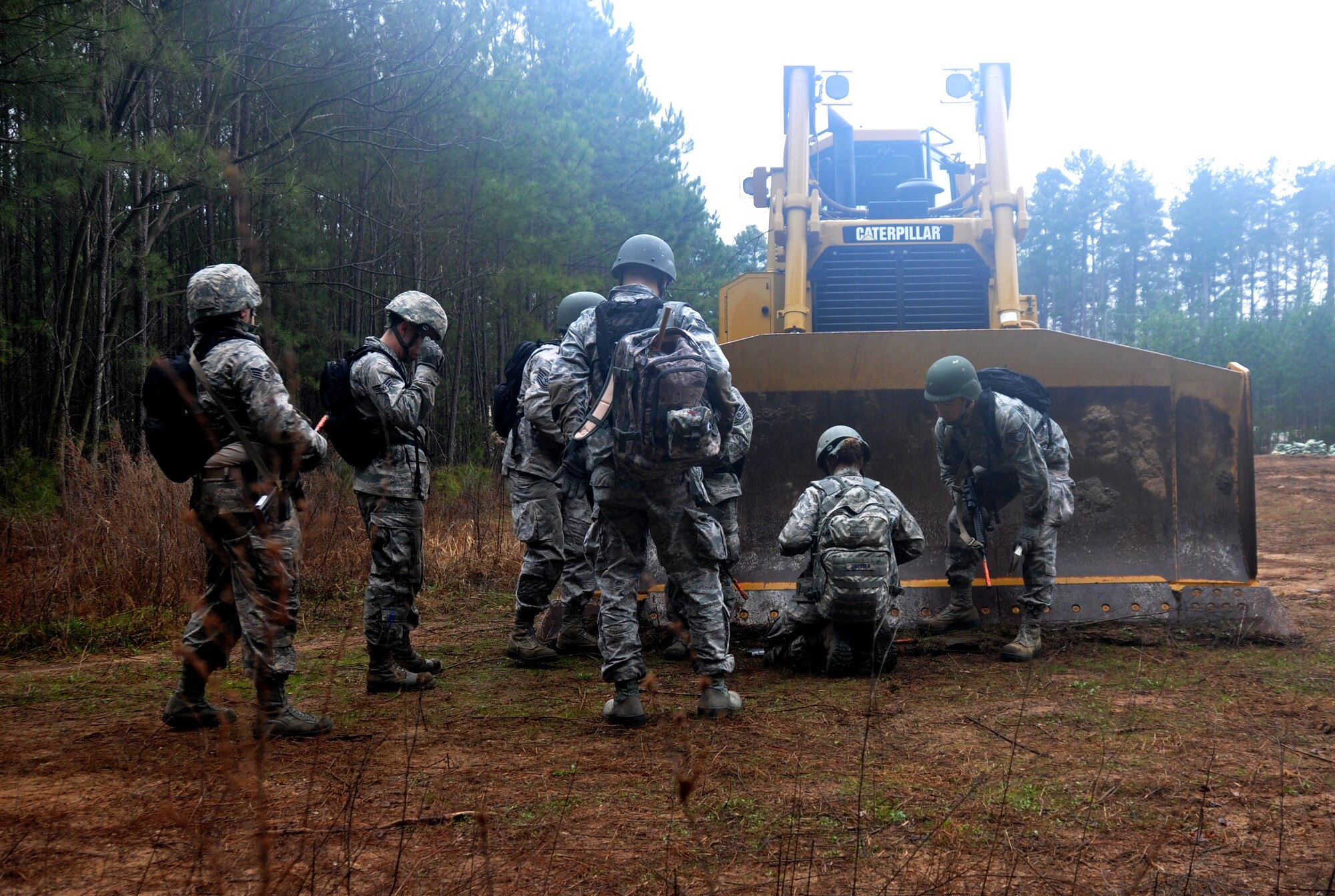 Airmen from the 911th Force Support Squadron, Pittsburgh, Pa., react to an attack by taking cover behind a bulldozer during OPERATION Everybody Panic as part of Force Support Silver Flag at Dobbins Air Reserve Base, Ga., March 10, 2015. Teams were tasked with engaging targets, self-aid buddy care, providing care under fire, identifying unexploded ordnances and improvised explosive devices, describing and providing the location of the UXOs and IEDs on a grid, low and high crawling, and transporting remains during this scenario. (U.S. Air Force photo/Senior Airman Daniel Phelps)