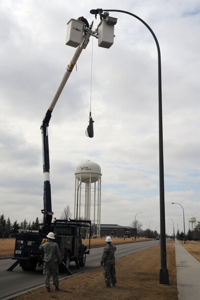 A crew from the 319th Civil Engineer Squadron replace streetlight fixtures on Grand Forks Air Force Base, N.D., March 19, 2015. Old high-pressure sodium bulbs such as the one being lowered are being replaced with energy-saving LED fixtures. (U.S. Air Force photo/Staff Sgt. David Dobrydney)