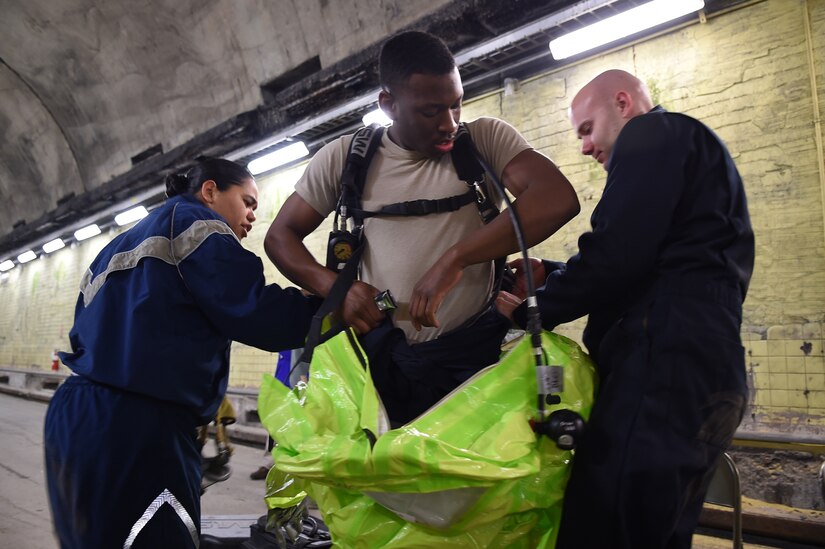Senior Airman Tony Pauline (center), gets geared up for a chemical agent training exercise with help from Staff Sgt. Yaoska Quintana (left) and Staff Sgt. Jonathan Moroz (right) in the Memorial Tunnel at the Center for National Response in Gallagher, WV., March 17, 2015. All three Airmen are members of the 779th Aerospace Medical Squadron at Joint Base Andrews, Md. (U.S. Air Force photo/Airman 1st Class Joshua R. M. Dewberry) 
