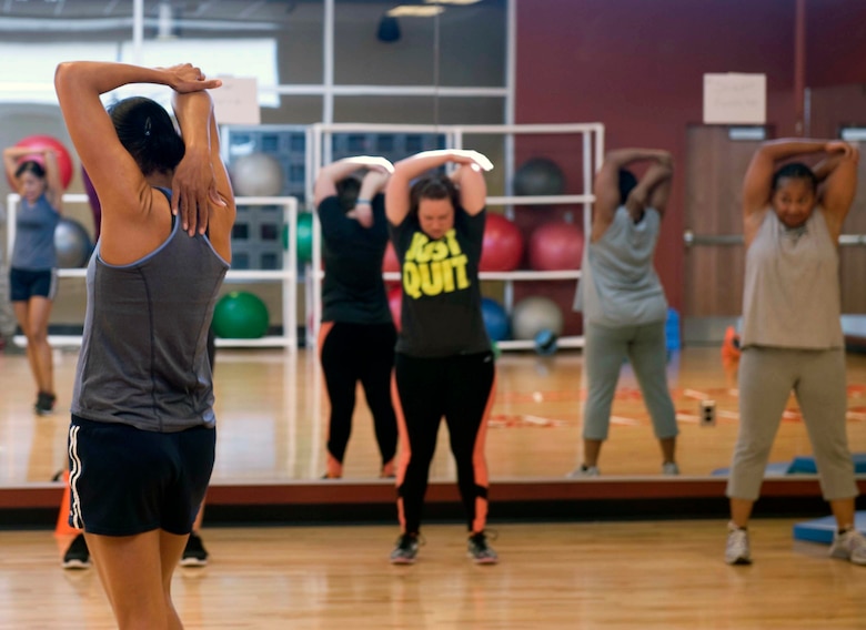 Nikki Harris (left) Warrior Fitness Center fitness instructor, leads her group fitness class into various sets of stretches at the fitness center on Nellis Air Force Base, Nev., Feb. 25, 2015. Harris spends her day administering fitness assessments, assisting those who may need to help getting on a regular exercise program, teaching group fitness classes, helping individuals quit smoking as well as teaching the six week run program. (U.S. Air Force photo by Airman 1st Class Rachel Loftis)