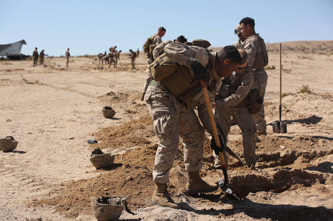 Cpl. Kagney W. Alexander, center, field artillery cannoneer, Battery A, Ground Combat Element Integrated Task Force, digs a skirmisher pit as one of the tasks during the Marine Corps Operational Test and Evaluation Activity assessment at Gun Position Quackenbush, Marine Corps Air Ground Combat Center Twentynine Palms, California, March 4, 2015. . From October 2014 to July 2015, the GCEITF will conduct individual and collective level skills training in designated ground combat arms occupational specialties in order to facilitate the standards-based assessment of the physical performance of Marines in a simulated operating environment performing specific ground combat arms tasks. (U.S. Marine Corps photo by Lance Cpl. Manuel R. Benavides/Released)