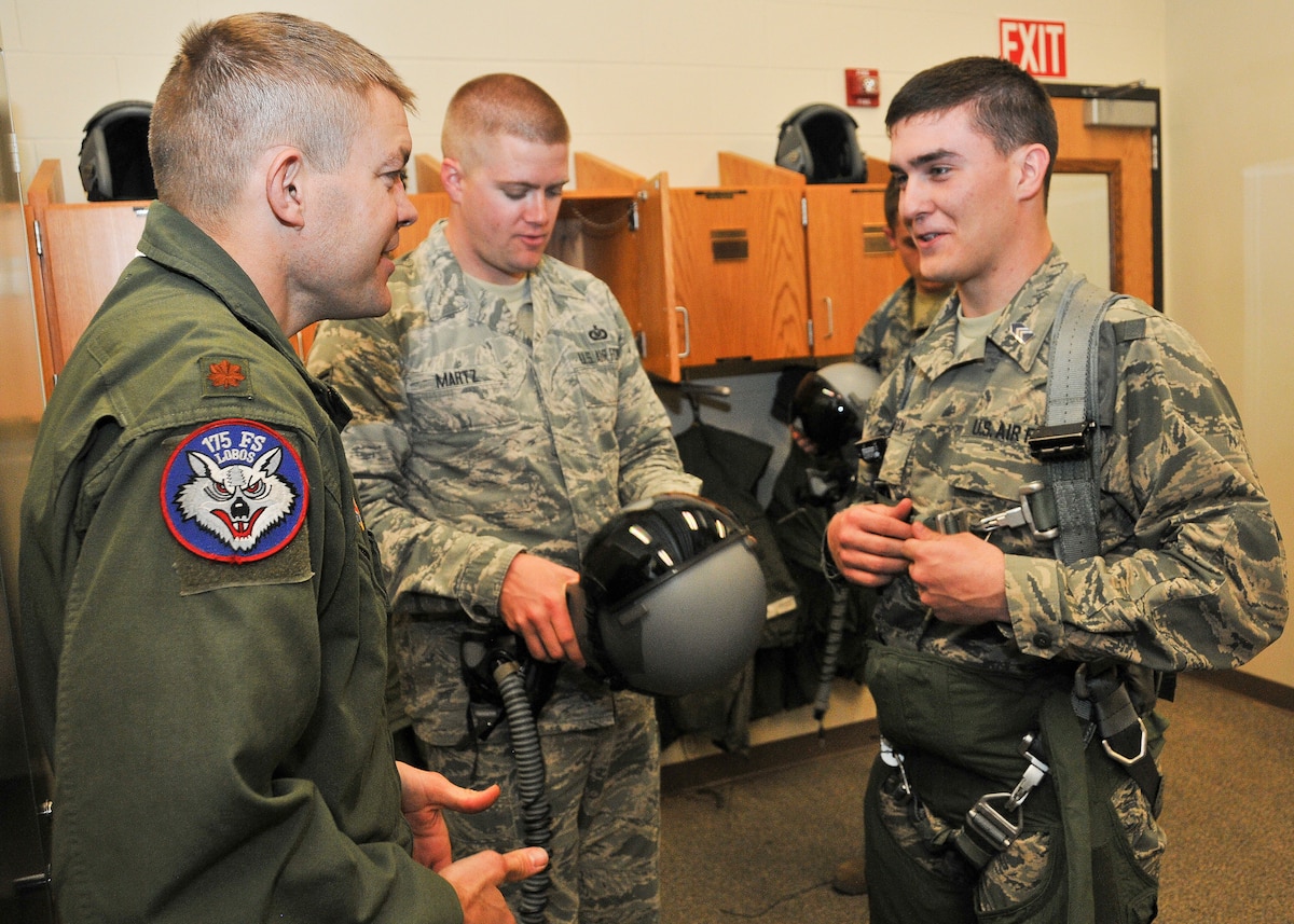 Maj. Karl Palmberg, 175th Fighter Squadron pilot, explains how to don a flight suit before a takeoff to Cadet 3rd Class Cole Jorgensen, South Dakota State University ROTC student, at Joe Foss Field, March 19, 2015. Jorgenson, a sophomore at SDSU, and more than 30 fellow cadets toured the 114th Fighter Wing and were briefed about the many roles and specialized fields that make up the South Dakota Air National Guard.(National Guard photo by Staff Sgt. Luke Olson/Released)