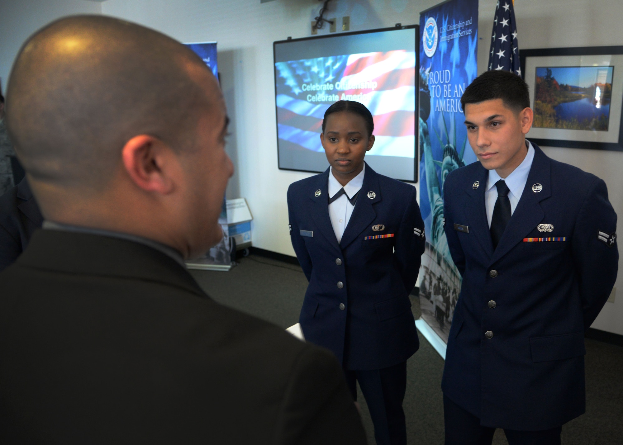 A representative from the United States Citizenship and Immigration Services field office in Albuquerque, New Mexico, speaks to U.S. Air Force Airman 1st Class Dominik Green, 27th Special Operations Logistics Readiness Squadron storage and issue specialist, and Airman 1st Class Rehema Mburugu, 27th Special Operations Contracting Squadron contract specialist, during a naturalization ceremony March 20, 2015 at Cannon Air Force Base, N.M. Four applicants were presented with their U.S. citizenship, representing four countries of origin during the ceremony. (U.S. Air Force photo/Staff Sgt. Alex Mercer)
