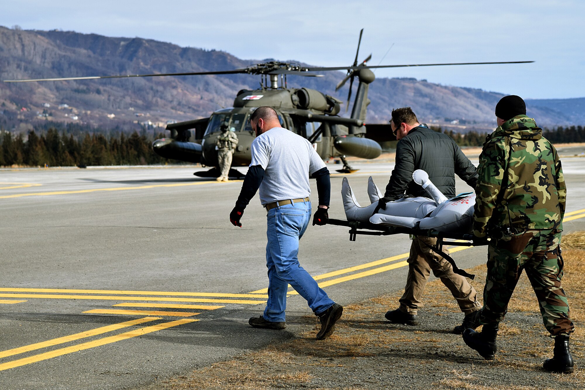 Civilian emergency responders carry a patient to a waiting USARAK Black Hawk helicopter as part of Exercise Rock and a Hard Place. The exercise scenario called for state and federal resources respond to assist the community of Homer and the Kenai Borough following a significant mudslide that damaged the South Peninsula Hospital and severed road and communications lines. The mass casualty-causing event required the rapid medical response of the State's Health and Social Services emergency response capabilities and the movement of patients from the damaged hospital to the Central Peninsula Hospital in Soldotna, Alaska. (U.S. Army photo/John Pennell)