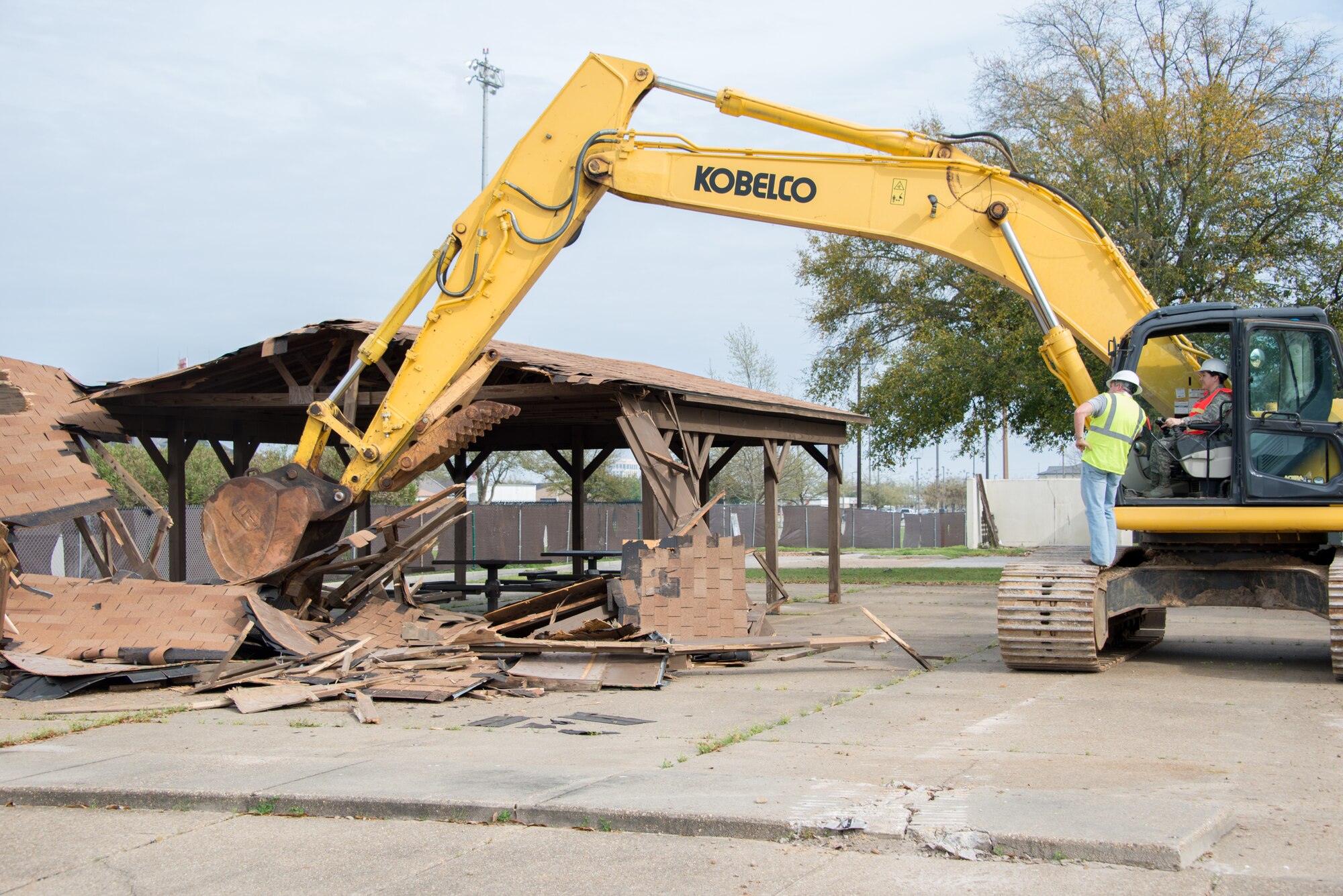 Capt. Veronica Williams, 81st Training Wing executive officer, and Jamie Bean, base operations support contractor, operate an excavator to begin the demolition of Hewes Hall, March 18, 2015, at Keesler Air Force Base, Miss. The prime demolition contractor is Bean Excavating. Brig. Gen. Patrick Higby, 81st Training Wing commander, loaned Williams his hard hat when he surprised her on-scene by asking her to participate in the demolition. (U.S. Air Force photo by Marie Floyd)