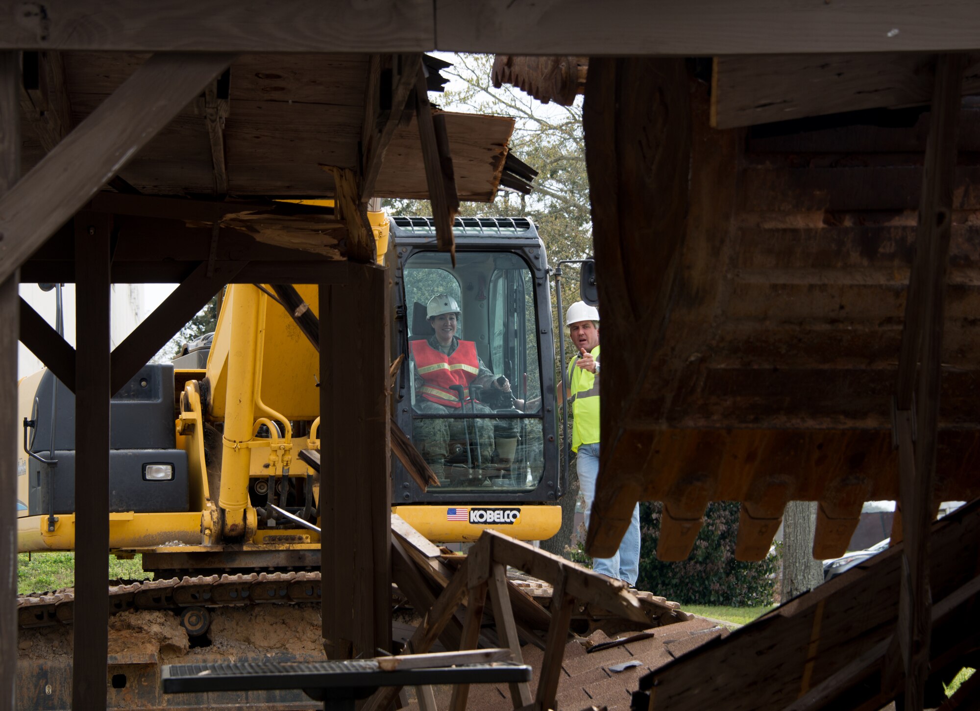 Capt. Veronica Williams, 81st Training Wing executive officer, and Jamie Bean, base operations support contractor, operate an excavator to begin the demolition of Hewes Hall, March 18, 2015, at Keesler Air Force Base, Miss. The prime demolition contractor is Bean Excavating. Brig. Gen. Patrick Higby, 81st Training Wing commander, loaned Williams his hard hat when he surprised her on-scene by asking her to participate in the demolition. (U.S. Air Force photo by Marie Floyd)