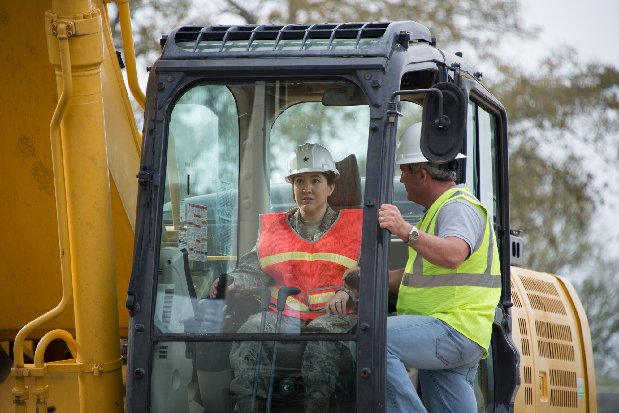Capt. Veronica Williams, 81st Training Wing executive officer, and Jamie Bean, base operations support contractor, operate an excavator to begin the demolition of Hewes Hall, March 18, 2015, at Keesler Air Force Base, Miss. The prime demolition contractor is Bean Excavating. Brig. Gen. Patrick Higby, 81st Training Wing commander, loaned Williams his hard hat when he surprised her on-scene by asking her to participate in the demolition. (U.S. Air Force photo by Marie Floyd)