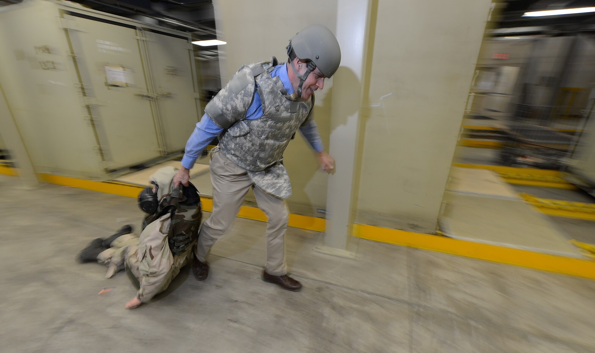 While wearing heavy combat protective equipment in the form of a ballistic vest and Kevlar helmet, Dr. John Spieker, 436th Aerospace Medical Squadron honorary commander, quickly pulls a training dummy through a warehouse during a skills test during a tour of the 436th Mission Support Group March 18, 2015, on Dover Air Force Base, Del. Honorary commanders were processed through a deployment line to become familiar with the amount and types of equipment deploying Airmen receive. (U.S. Air Force photo/Greg L. Davis)