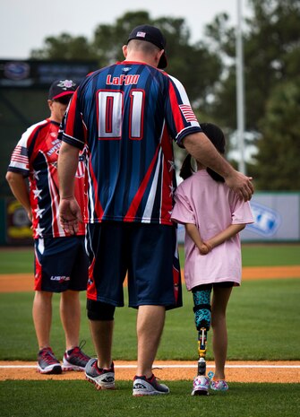 Gary LaFon, Wounded Warrior Amputee Softball Team coach, walks a young girl out on to the field to stand with the WWAST members for the national anthem March 21, 2015, at Joe Riley Stadium in Charleston, S.C. The WWAST is a charitable organization whose mission is to raise awareness, educate and inspire the public about the strength and resiliency of the wounded warriors. The WWAST accomplish their mission by showing how a positive attitude, commitment, dedication and perseverance enable them to overcome any obstacle. (U.S. Air Force photo/Airman 1st Class Clayton Cupit)