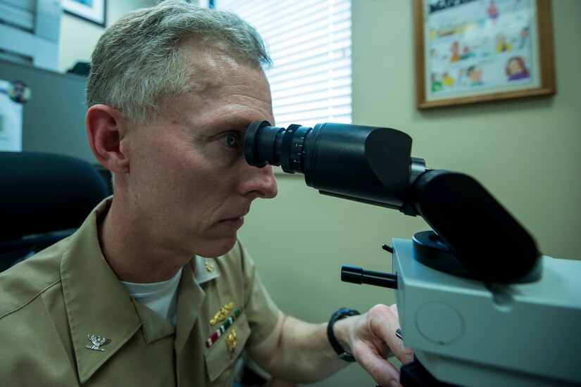 Navy Capt. George Butler looks at slides on his microscope in his office March 13, 2015  at the Naval Health Clinic Charleston, S.C. Since Fiscal Year 2012, Butler has been the Navy's top producing dermatologist. Butler is the staff dermatologist at NHCC. (U.S. Air Force photo / Senior Airman Jared Trimarchi)
