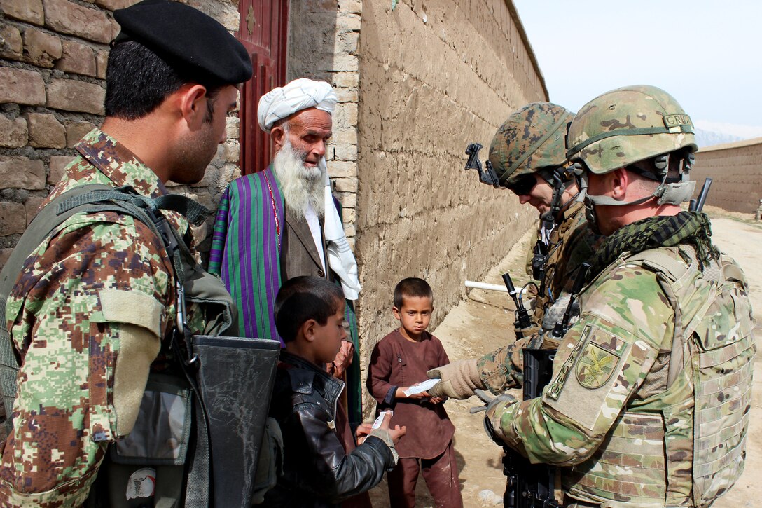A U.S. soldier, Marine, Georgian soldier and Afghan army soldier talk with local villagers and hand the children candy bars during a patrol outside of the Qaleh Musa Pain village in Helmand province, Afghanistan, March 12, 2015.