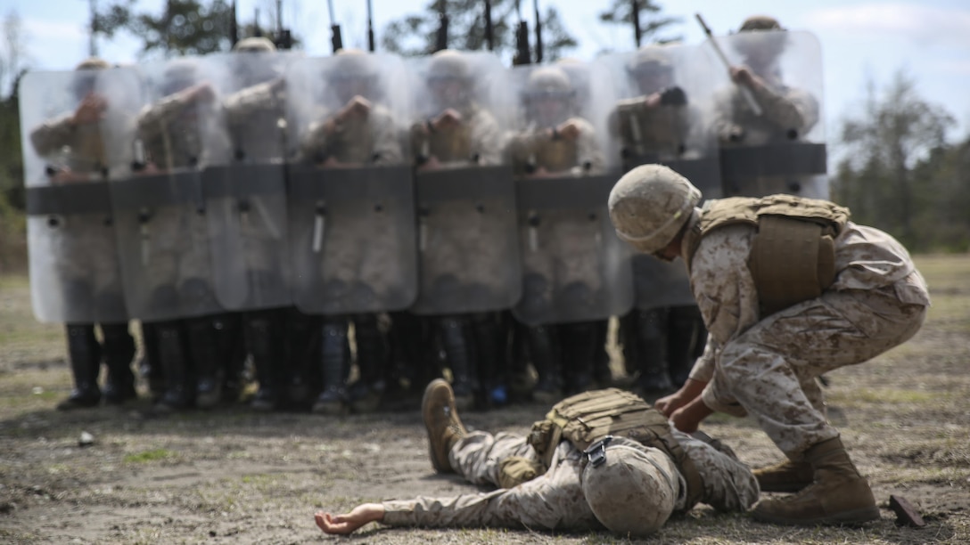 Marines with Battery and Golf Co., 2nd Battalion, 6th Marines, acting as role-players, stand guard around a mock casualty during a riot control exercise aboard Camp Lejeune, N.C., March 24, 2015. Staff Sgt. Shawn J. Dyer, the lead non-lethal weapons instructor with Expeditionary Operations Training Group, II MEF, said, “You have to work in unison, moving together in step with the shields and firing the weapons.” 