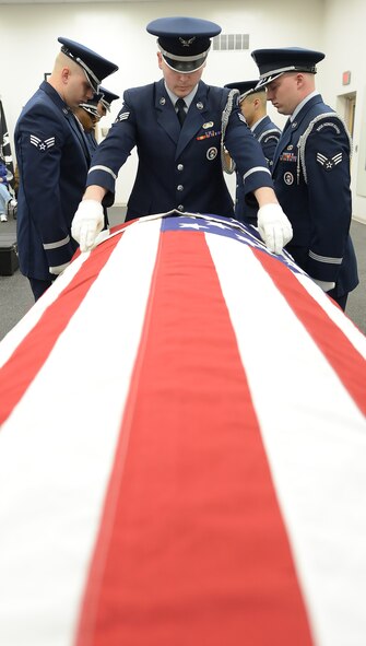 Senior Airman Kellenberger, center, Dover Air Force Base Honor Guard, inspects the American flag draped over a training coffin during a 436th Mission Support Group mission capabilties demonstration for the 2015 Honorary Commanders March 18, 2015, on Dover Air Force Base, Del. Also prominitely shown are Senior Airman James Korte, left, and SrA Lance Wright, right.  (U.S. Air Force photo/Greg L. Davis) 