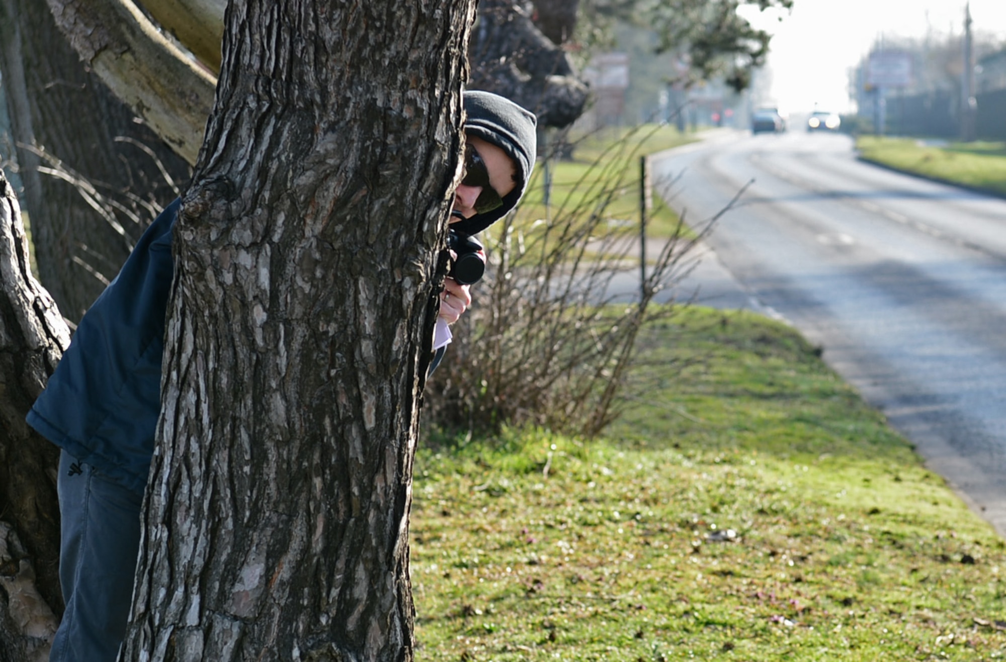 Senior Airman Trenton Hawk, 48th Civil Engineer Squadron, pretends to takes photos of vehicles as they pass by Gate 2 at Royal Air Force Lakenheath, England, March 12, 2015. Trenton was behaving suspiciously as part of an Eagle Eyes exercise the 48th Fighter Wing Inspection Team held to test the vigilance of the base populace. (U.S. Air Force photo by Airman 1st Class Erin R. Babis/Released)