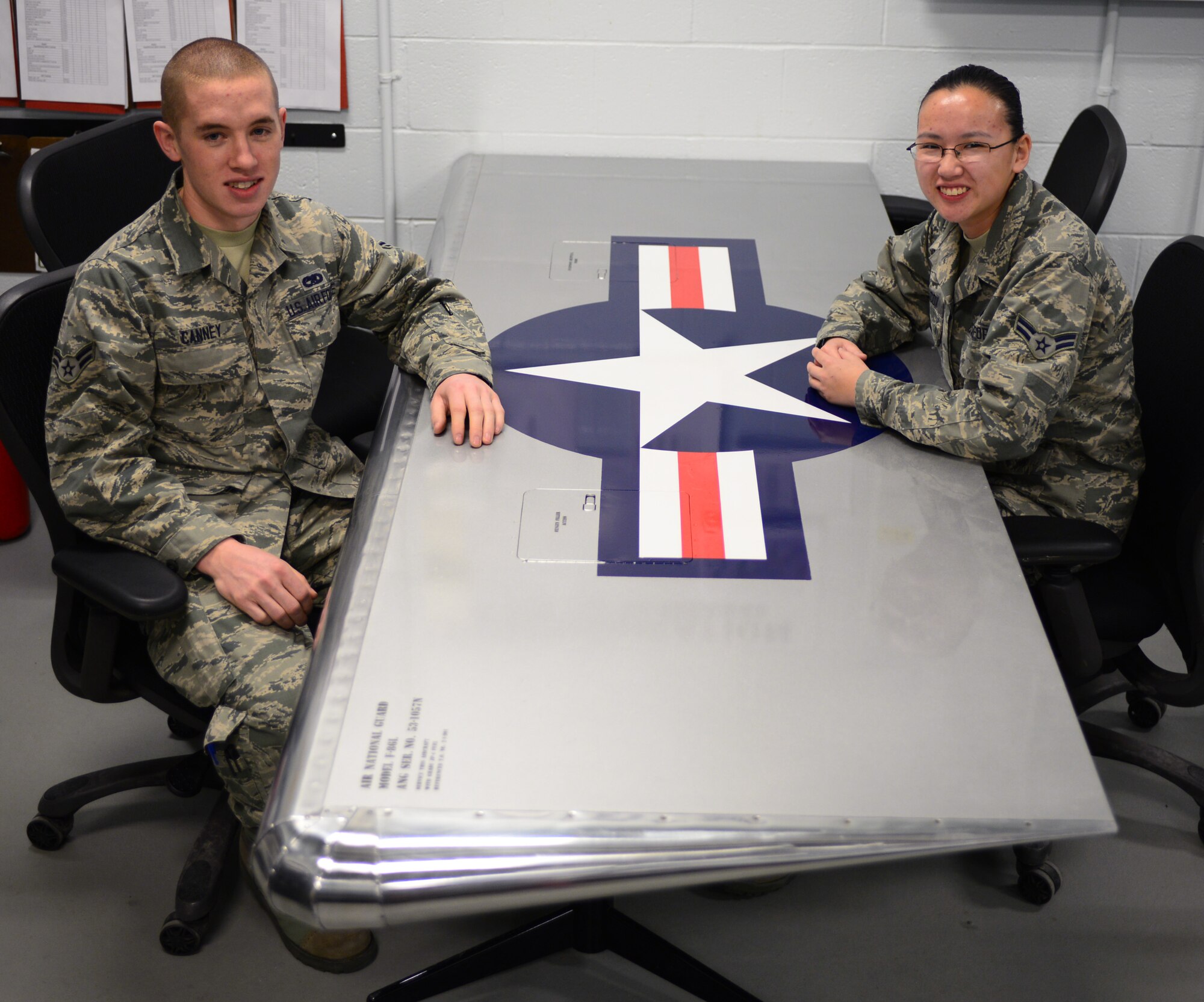 New Hampshire Air National Guard Airman First Class Kevin Canney (left) and Airman First Class Margaret Wilcox, both aircraft structural maintenance apprentices with the 157th Maintenance Group, sit at the aircraft wing shaped table they designed, built and painted March 24, 2015 Pease Air National Guard Base, N.H. They made the table to practice the skills they learned in technical school before working on actual aircraft. (New Hampshire Air National Guard photo by Airman Ashlyn J. Correia/RELEASED)