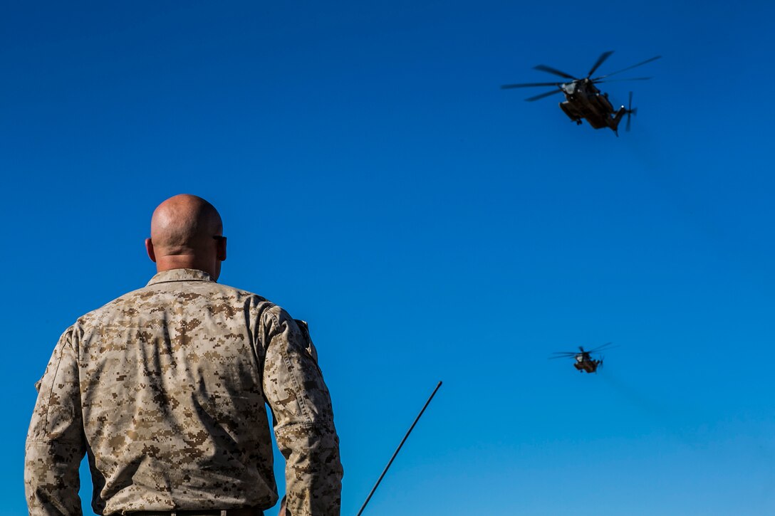 U.S. Marine Corps Sgt. David W. Berry, a helicopter rope suspension technique master attending the infantry officers course, observes CH-53-E Super Stallions fly overhead prior to a fast rope training exercise in preparation for Talon Reach during Weapons and Tactics Instructor Course (WTI 2-15) at Auxiliary Airfield 2 near Yuma, AZ., March 26, 2015. WTI is a seven-week event hosted by Marine Aviation Weapons and Tactics Squadron One (MAWTS-1) cadre. MAWTS-1 provides standardized tactical training and certification of unit instructor qualifications to support Marine aviation Training and Readiness and assists in developing and employing aviation weapons and tactics. (U.S. Marine Corps photo by Lance Cpl. Jodson B. Graves 2d MAW Combat Camera/Released)