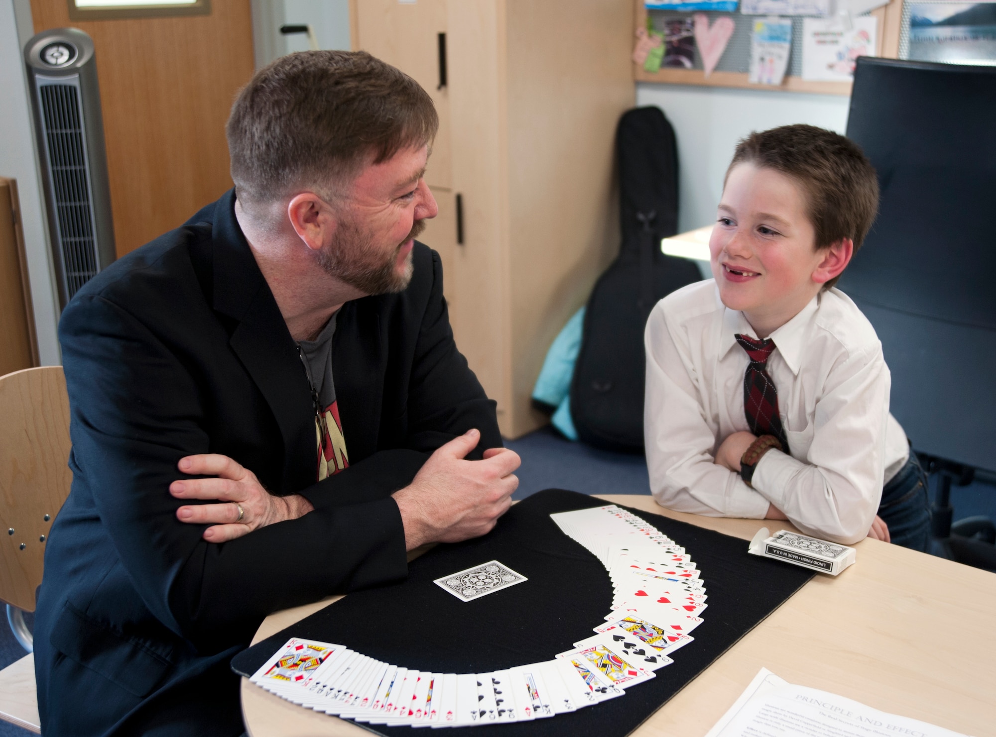 Richard Kennedy, 59th Signal Battalion information specialist magician, teaches a card trick to Blaze Byrne, son of Brent Byrne, Amerisafe safety engineer, at the Illa School Age Program on Joint Base Elmendorf-Richardson, Alaska, March 20, 2015. Kennedy teaches his classes the basics of magic, from disappearing acts to simple illusions the children can practice at home. (U.S. Air Force photo/Airman 1st Class Tammie Ramsouer)