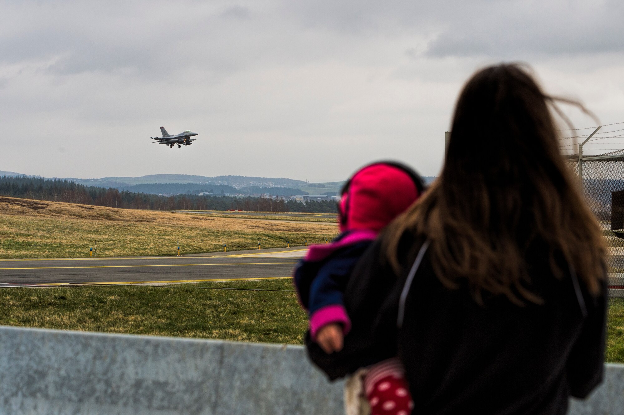 The spouse of a 480th Fighter Squadron member witnesses the arrival of an F-16 Fighting Falcon fighter aircraft pilot assigned to it land on the runway at Spangdahlem Air Base, Germany, March 27, 2015. A total of six aircraft returned from participating in Dacian Warhawk 2015, a bilateral flying training deployment with the Romanian air force. (U.S. Air Force photo by Staff Sgt. Christopher Ruano)