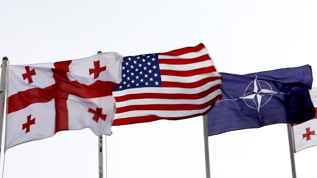 The national colors of Georgia and the United States, along with the NATO flag, wave above a parade deck before a departure ceremony for Georgian soldiers and U.S. Marines headed to Afghanistan, March 24, Vaziani Training Area, Georgia. Over the last six months, the Georgia Deployment Program – Resolute Support Mission prepared the Georgian 43rd Light Infantry Battalion and U.S. Marine advisors for NATO’s Resolute Support in Afghanistan.