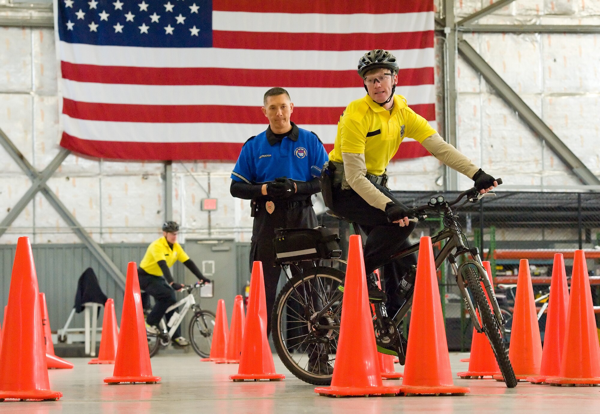 Corporal Allen Hawk, Ocean City Police Department, Md. center, observes Senior Airman Jordan Hucks, 436th Security Forces Squadron response force leader, right, navigate his mountain bike around two cones centered in a box-shaped area March 19, 2015, at Dover Air Force Base, Del. Hucks accomplished both clockwise and counter-clockwise versions of this slow-speed, confined area bike test taught by Hawk, an International Police Mountain Bike Association certified instructor. (U.S. Air Force photo/Roland Balik)