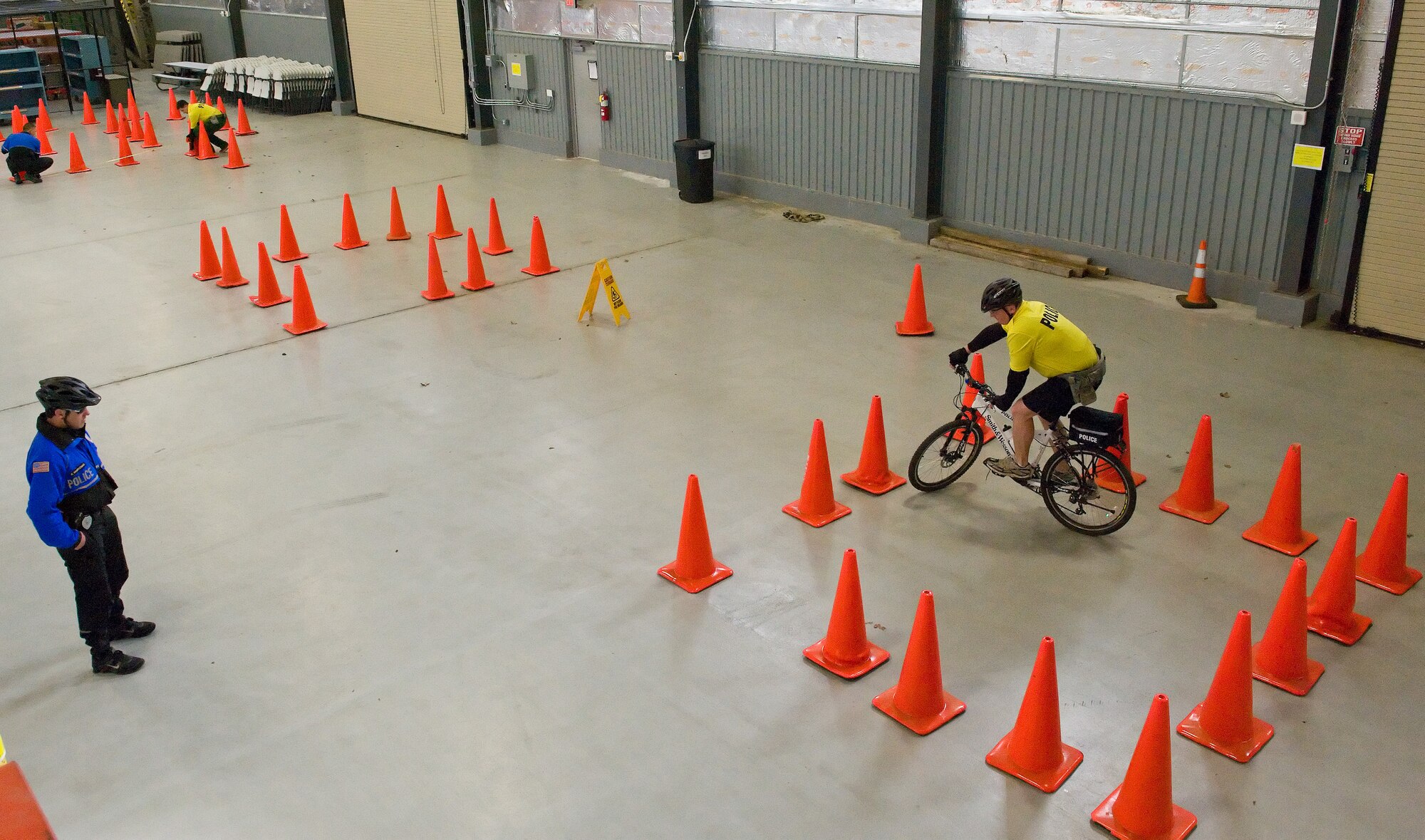 Corporal Richard Wawrzeniak, Ocean City Police Department, Md. left, observes Staff Sgt. Bryan Miller, 436th Security Forces Squadron security forces trainer, right, ride his mountain bike within a box-shaped area March 19, 2015, at Dover Air Force Base, Del. Miller accomplished both clockwise and counter-clockwise versions of this confined area slow-speed riding skills test, as well as other tests required to pass the riding portion of the police bike patrol course taught here, March 16-19. (U.S. Air Force photo/Roland Balik)