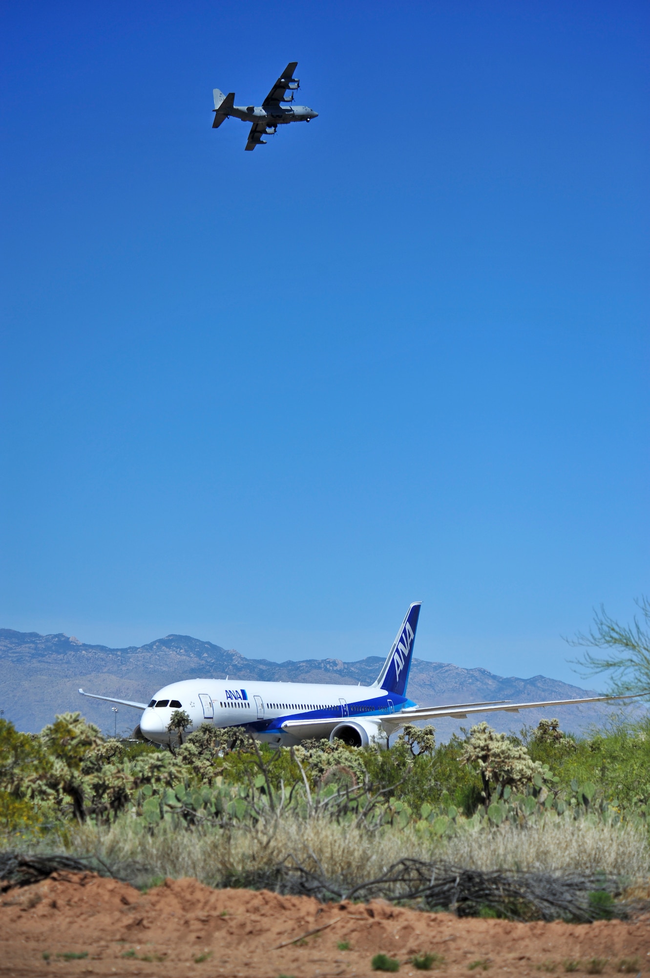A Boeing 787-8 Dreamliner is towed on a newly widened road to Pima Air & Space Museum as an EC-130H Compass Call flies overhead at Davis-Monthan Air Force Base, Ariz., March 26, 2015.  The 355th Civil Engineer Squadron used this opportunity to conduct training on creating and paving roads; skills which are necessary to have in deployed locations.   (U.S. Air Force photo by Airman 1st Class Chris Massey/Released)