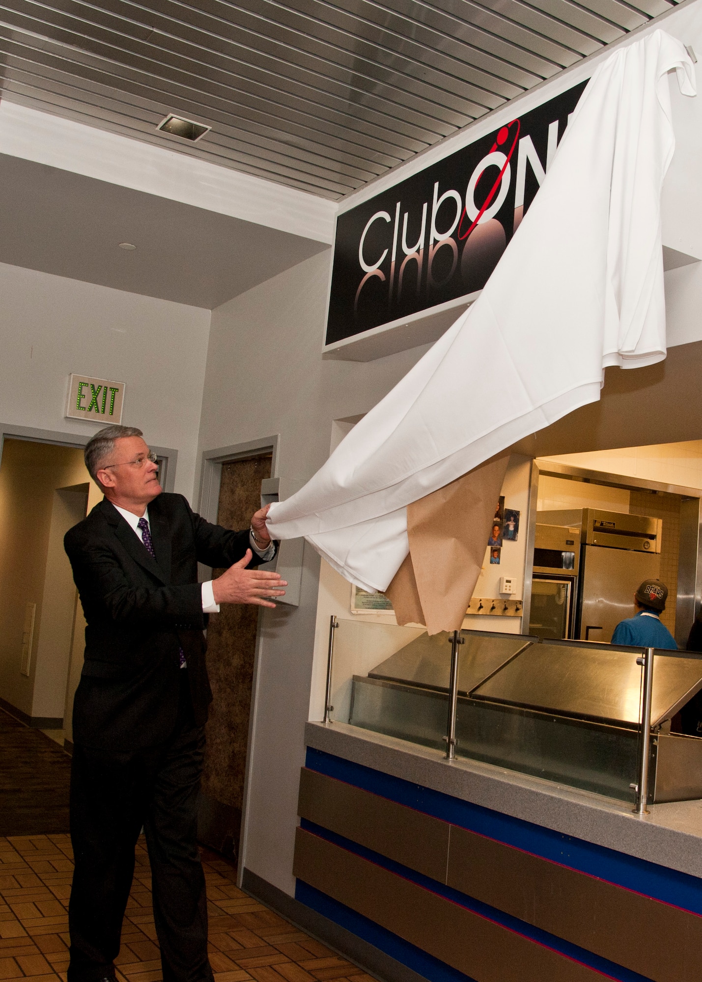 PETERSON AIR FORCE BASE, Colo. – Scott Anderson, Air Force Space Command A4/7 director, reveals the name of Club One, the newly remodeled and renamed Air Force Space Command snack bar, during the grand opening March 18. The event included a pizza buffet provided by the Colorado Pizza Company along with a raffle for prizes to the golf course, bowling center and other on-base facilities. Club One is open from 7 a.m.–1:30 p.m. Monday-Friday, and among its selection offers eggs, bacon, pancakes and breakfast burritos in the morning, while serving a variety of hot and cold sandwiches, burgers, soups, a daily salad bar and many other options. (U.S. Air Force photo by Staff Sgt. J. Aaron Breeden)
