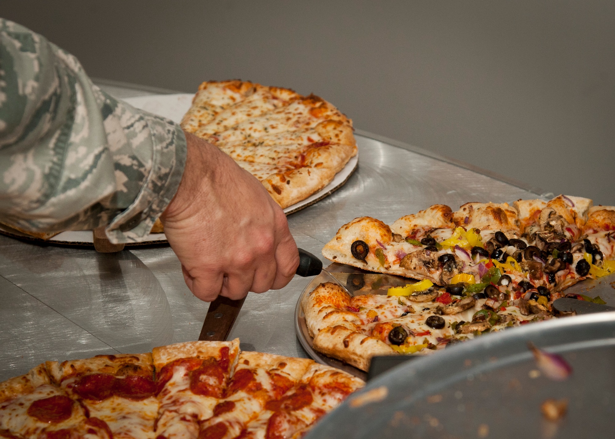 PETERSON AIR FORCE BASE, Colo. – A patron reaches for a slice of pizza during the grand opening of Club One, the newly remodeled and renamed Air Force Space Command snack bar, March 18. The event included a pizza buffet provided by the Colorado Pizza Company along with a raffle for prizes to the golf course, bowling center and other on-base facilities. Club One is open from 7 a.m.–1:30 p.m. Monday-Friday, and among its selection offers eggs, bacon, pancakes and breakfast burritos in the morning, while serving a variety of hot and cold sandwiches, burgers, soups, a daily salad bar and many other options. (U.S. Air Force photo by Staff Sgt. J. Aaron Breeden)