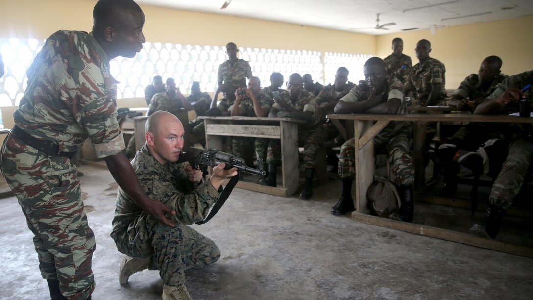 U.S. Marine Cpl. Christopher Moore, a machine gunner with Special-Purpose Marine Air-Ground Task Forces Crisis Response-Africa, demonstrates the proper kneeling position with the help of an interpreter during a marksmanship class for the Cameroonian Naval Commando Company, near Limbe, Cameroon, March 12, 2015. Moore is part of a Theater Security Cooperation team, which traveled to Cameroon to conduct an engagement focused on marksmanship and other basic infantry skills with the COPALCO during the multinational maritime security exercise, Africa Partnership Station. (Official U.S. Marine Corps photo by Staff Sgt. Steve Cushman/Released)