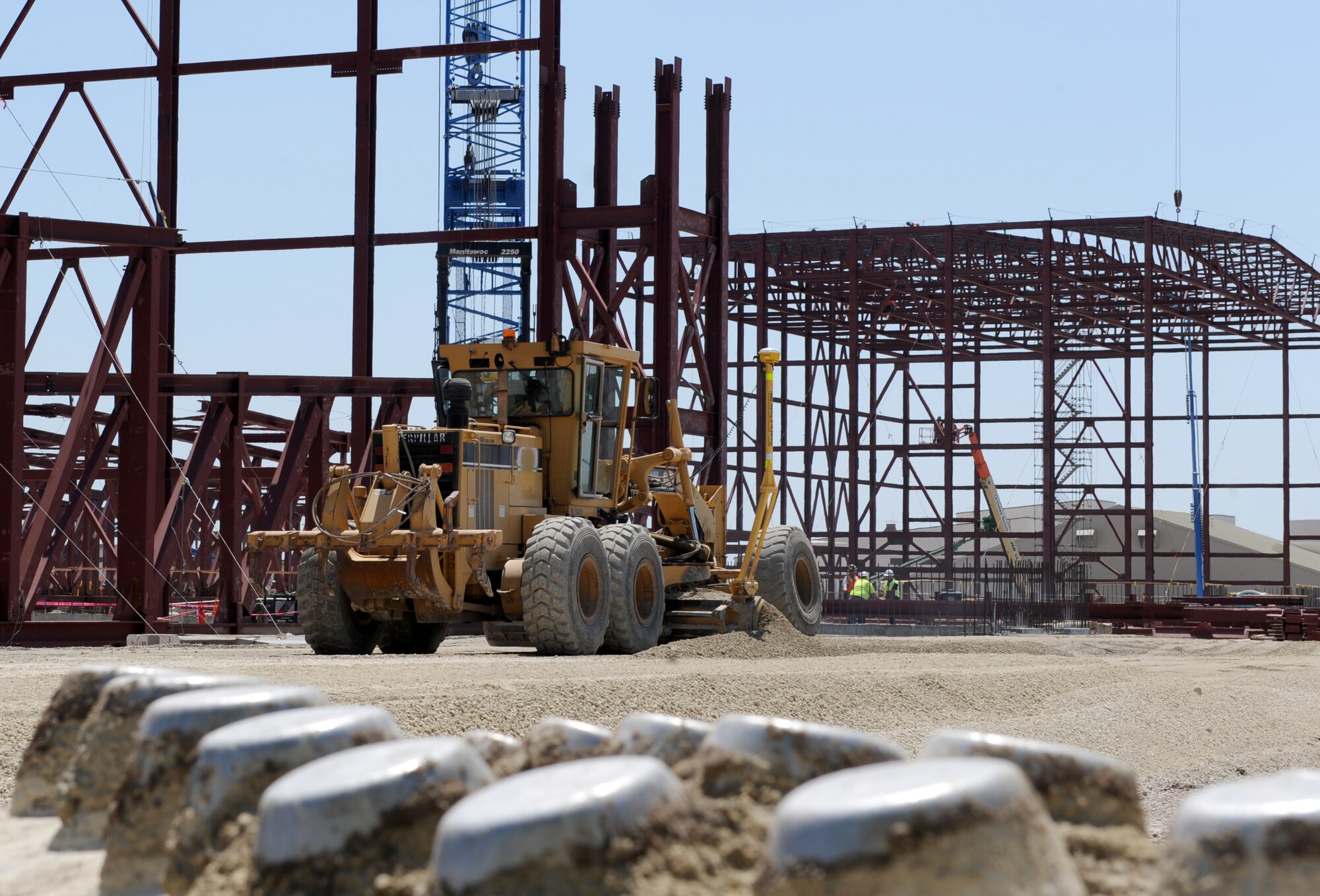 A road grater spreads gravel in front of Hangar 1124, April 30, 2015, at McConnell Air Force Base, Kan. The gravel is needed to make a foundation to support the cranes that will hoist the next section of the roof onto the hangar. Hangar 1124 will be a dual function hangar with a bay for corrosion control and a second bay for fuel systems, both for the KC-46A Pegasus. (U.S. Air Force photo by Staff Sgt. Rachel Waller)