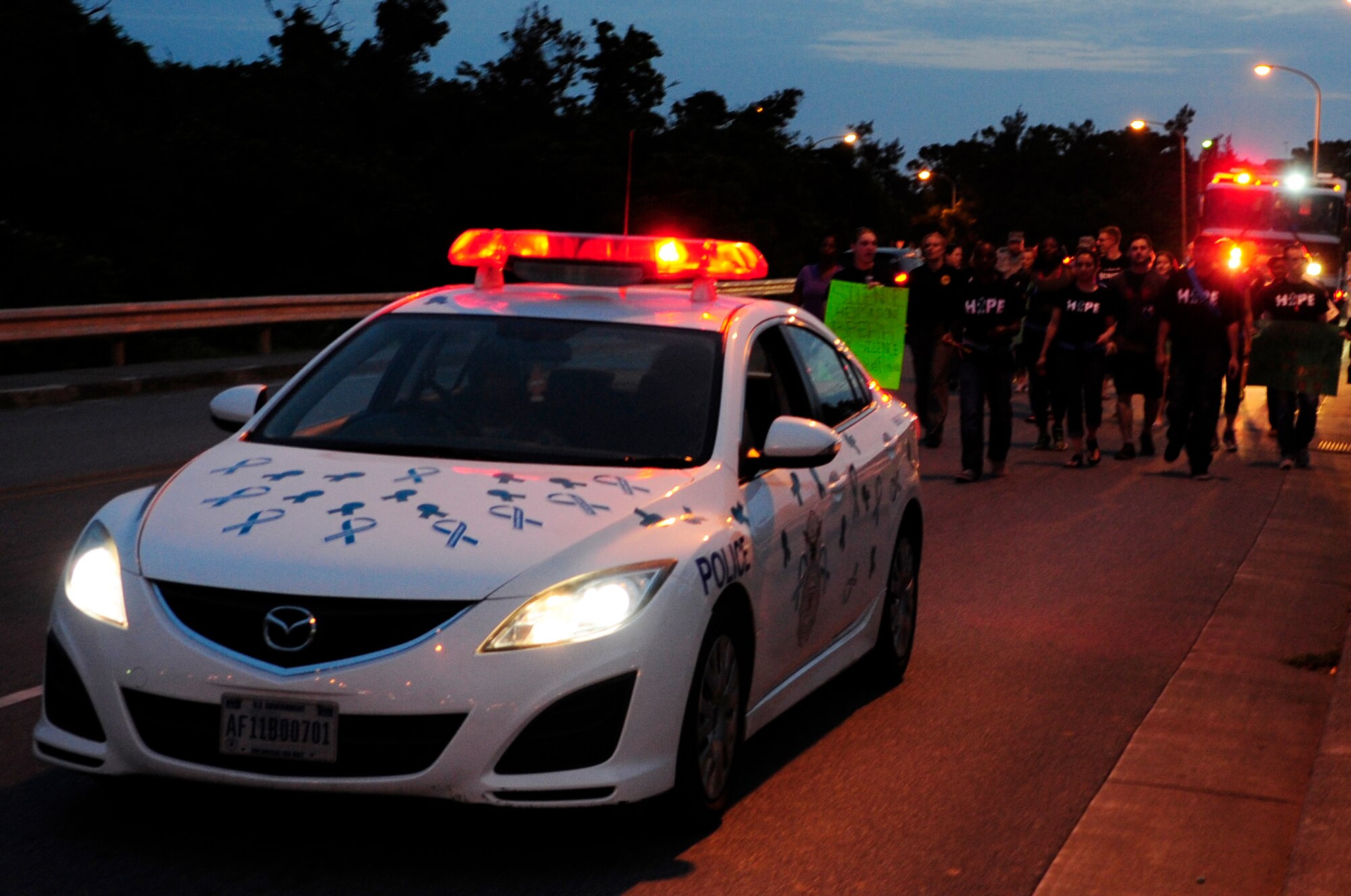 An 18th Wing Security Forces patrol car decorated in teal ribbons leads the Take Back the Night march on Kadena Air Base, Japan, May 1, 2015. The participants marched from the Schilling Community Center parking lot toward Chapel 2 with noise makers and cowbells, while chanting, symbolizing survivors reclaiming the night, the time when sexual assaults are most likely to occur. (U.S Air Force photo/Senior Airman Omari Bernard)