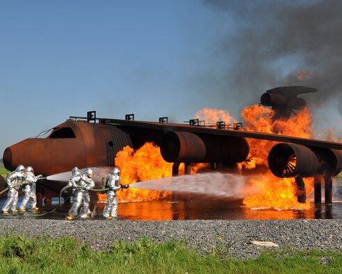 Firefighters from the 307th Civil Engineer Squadron at Barksdale Air Force Base, La., attack a controlled burn on an aircraft fire training simulator during the May Unit Training Assembly. Barksdale Air Force Base is one of the bases equipped with an aircraft fire training simulator allowing firefighters to recreate different emergency scenarios without burning up an aircraft every time they practice. (U.S. Air Force photo by Master Sgt. Laura Siebert/Released)