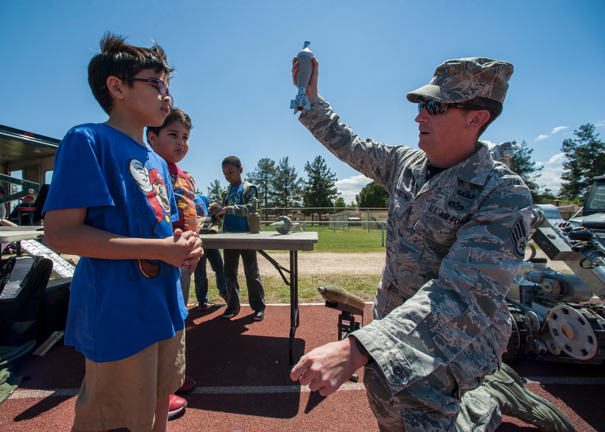 Staff Sgt. D’Augustino, 39th Civil Engineer Squadron explosive ordinance technician, explains the trajectory of rockets to Hyland, 39th Air Base Wing dependent, during the 2015 Job Shadow Day April 24, 2015, at Incirlik AB, Turkey. The 39th CES EOD team had an abundance of interactive training equipment for children to play with and try on. (U.S. Air Force photo by Airman 1st Class Cory W. Bush/Released)
