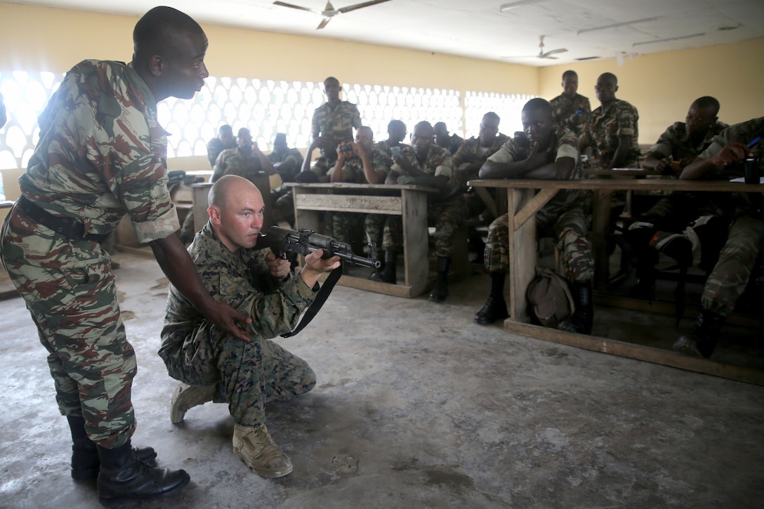 U.S. Marine Cpl. Christopher Moore, a machine-gunner with Special-Purpose Marine Air-Ground Task Forces Crisis Response-Africa, demonstrates the proper kneeling position with the help of an interpreter during a marksmanship class for the Cameroonian Naval Commando Company, near Limbe, Cameroon, March 12, 2015. Moore is part of a Theater Security Cooperation team, which traveled to Cameroon to conduct an engagement focused on marksmanship and other basic infantry skills with the COPALCO during the multinational maritime security exercise, Africa Partnership Station. (Official U.S. Marine Corps photo by Staff Sgt. Steve Cushman/Released)