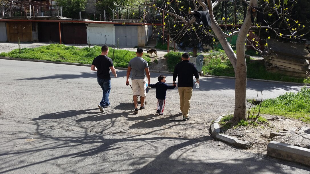 Corporal Jason A. Rigsby, Luka, Sgt. Fabien Melgar, and Cpl. Joseph C. Howard bring a load of trash to the dumpster after cleaning up the back yard. Marines of Georgia Deployment Program-Resolute Support Mission volunteered their time at KERA’s Women Shelter to help improve and maintain robust relationships with their local community while abroad.