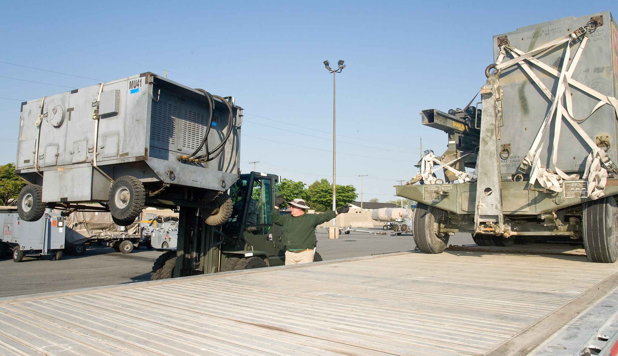 Ron Webb, a blocker, bracer and crane operator, marshals forklift operator Senior Airman Jacob Firgens, both from the 436th Aerial Port Squadron, during a cargo upload May 4, 2015, at the outsized cargo area on Dover Air Force Base, Del. Webb and Firgens positioned numerous items of rolling stock on a flatbed requiring transportation from Dover AFB. (U.S. Air Force photo/Roland Balik)