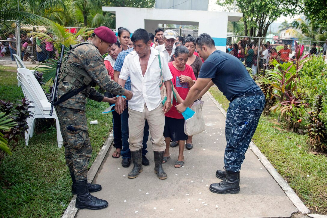 Guatemalan army Sgt. Kevyn Alexander Cruz Estrada, assigned to Brigida de Infanteria de Marina, and U.S. Navy Seaman David Vasquez tie wristbands on patients during Continuing Promise 2015 in Puerto Barrios, Guatemala, April 29, 2015. 