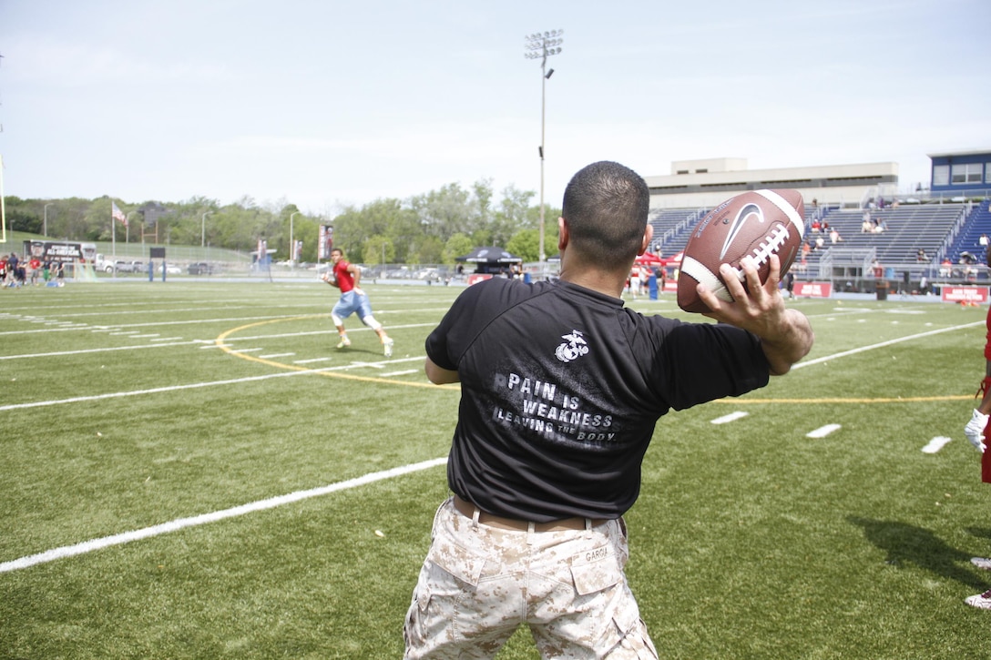 Sergeant Matthew Garcia, a Marine Corps Recruiting Station Kansas City recruiter, throws a football downfield to receivers as part of a route-running drill during the Semper Fidelis All-American Football Camp at Rockhurst High School's Vincent P. Dasta Memorial Stadium May 3, 2015.  