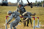 Soldiers leap over a barricade during the fallen comrade event at the Winston P. Wilson shooting matches held at Camp Joseph T. Robinson in North Little Rock, Ark., Oct. 24-29, 2010. The event had Soldiers run a total of 200 yards, while negotiating obstacles and carrying a dummy. In the middle of the event, they lie prone and knock down seven targets with rifle fire.