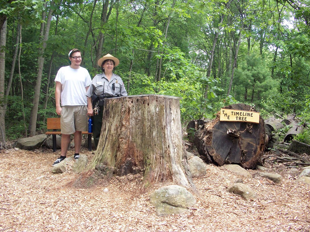 Boy Scout Brian DiPasquale and Park Ranger Viola Bramel stand at his Timeline Tree and bench project at the entrance of West Hill Dam, Uxbridge, Massachusetts. 