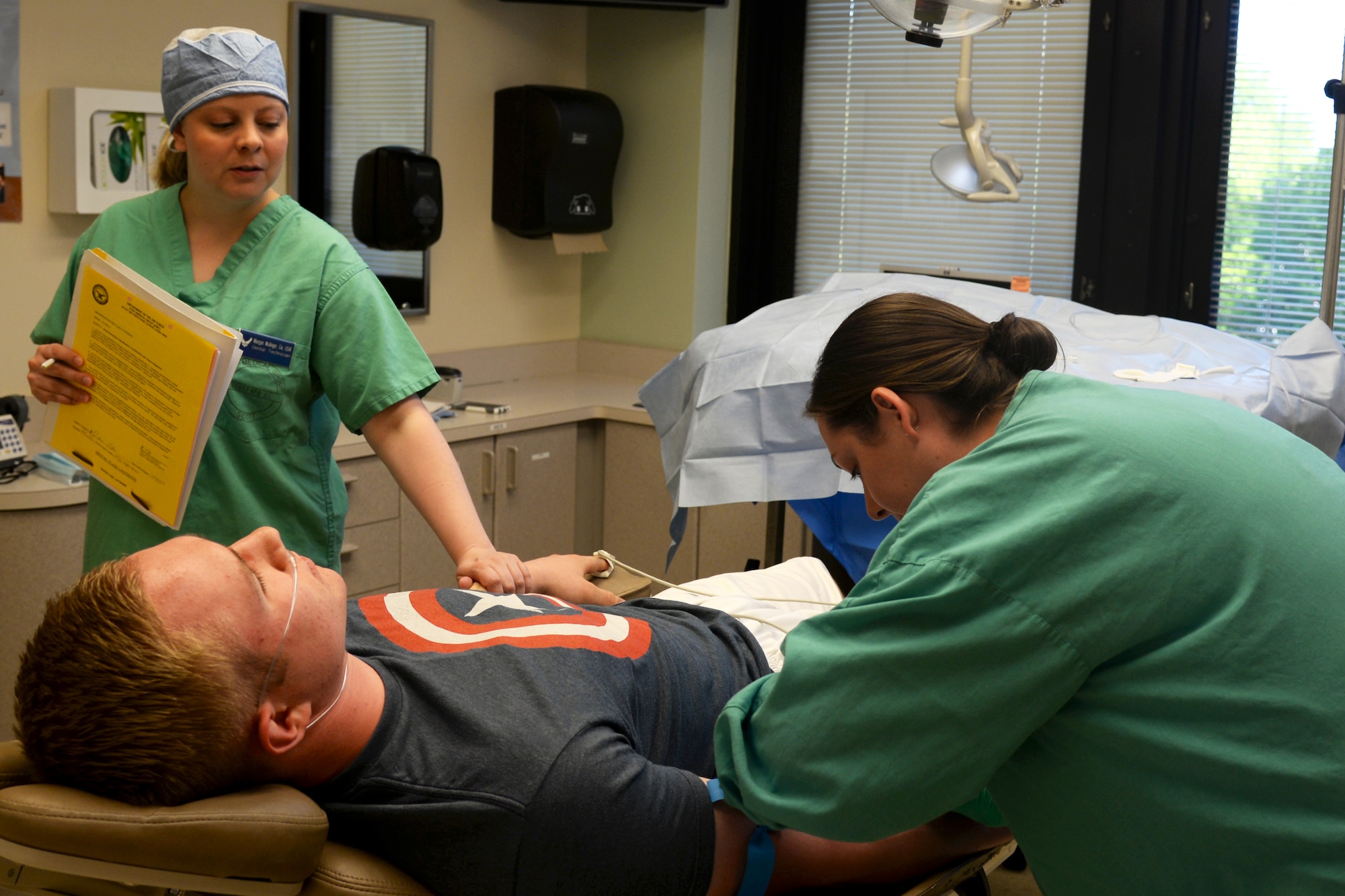 Staff Sgt. Brittany Lanahan inserts a needle into a patients arm to properly sedate a patient during a wisdom teeth extraction procedure as Maegan Wallinger comforts the patient at the 375th Medical Group Clinic at Scott Air Force Base, Illinois, April 29, 2015. Wisdom teeth are removied to correct or prevent future problems that may occur. Lanahan is the Oral Surgery NCOIC and Wallinger is a dental assistant from the 375th DS. (U.S. Air Force Photo by Airman 1st Class Megan Friedl)