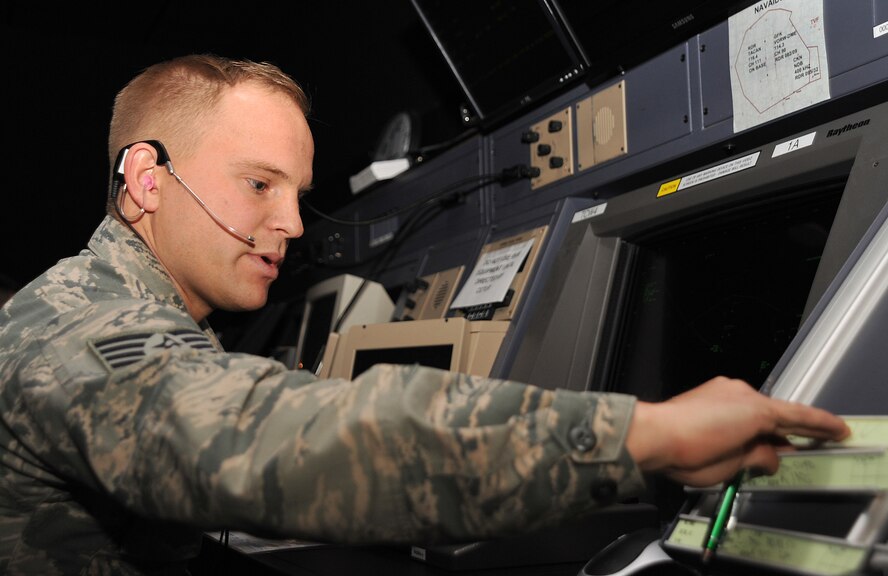 Staff Sgt. Aaron Waaraniemi, 319th Operations Support Squadron air traffic controller, fills out flight strips while communicating with training pilots from the University of North Dakota to set an arrival sequence for them as they prepare to land on Grand Forks Air Force Base, N.D., April 29, 2015. Flight strips are a written record of everything the controller tells an aircraft to do. (U.S. Air Force photo by Airman 1st Class Bonnie Grantham/Released)